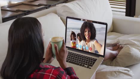 Mujer-Afroamericana-Sosteniendo-Una-Taza-De-Café-Haciendo-Una-Videollamada-En-Una-Computadora-Portátil-Sentada-En-El-Sofá-De-Casa