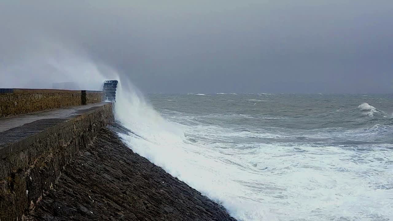 Waves crashing onto sea defences Porthcawl lighthouse South Wales during storm Atiyah in slow motion