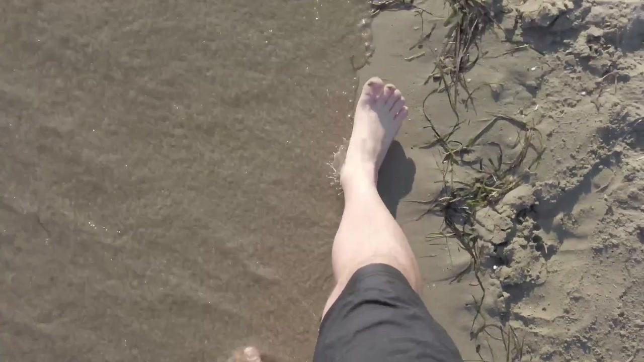 Point-of-view video looking down while walking across fine beach sand in Greece during summer.