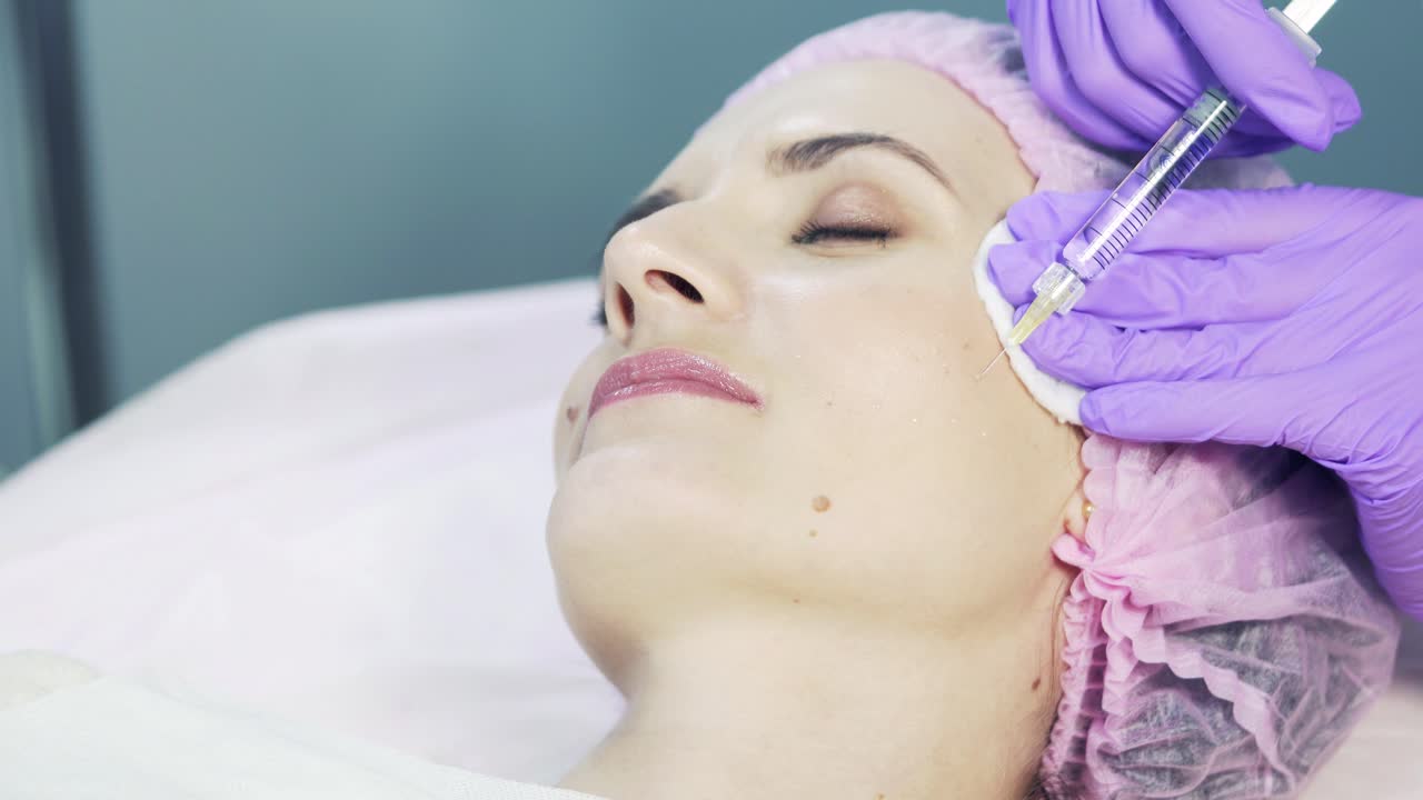 Cosmetologist s hands in gloves making face injection in beauty salon. Woman gets beauty facial cosmetology procedure.