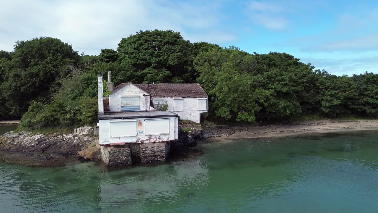 Abandoned Welsh coastal property aerial view circling idyllic turquoise Holyhead beach seascape