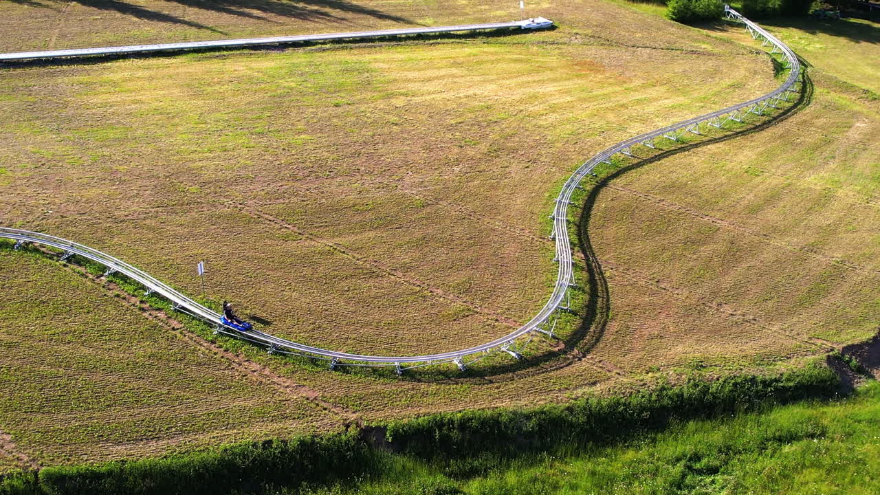 Aerial drone view of summer toboggan alpine coaster in the Carpathians in Romania. Hills covered with lush forest