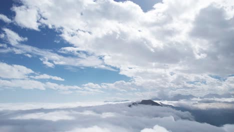 high altitude aerial drone view, flying above fluffy clouds and mountains