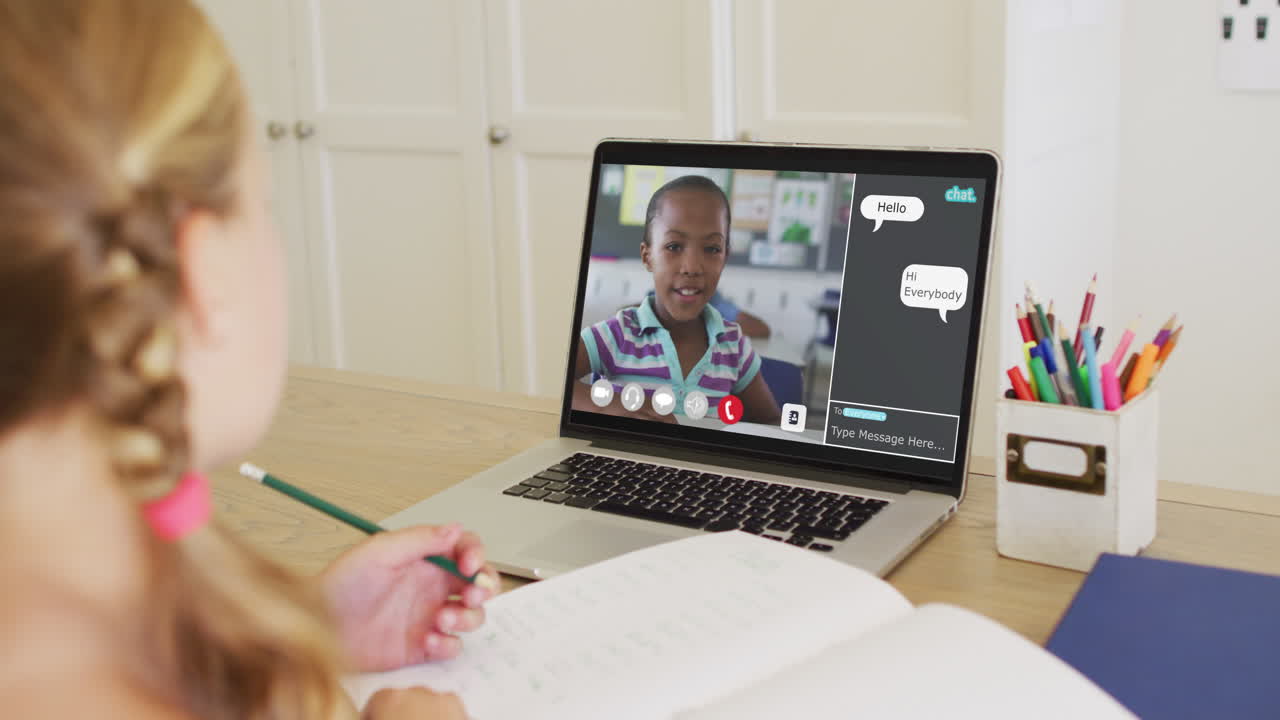 Schoolgirl using laptop for online lesson at home, with her school friend and web chat on screen