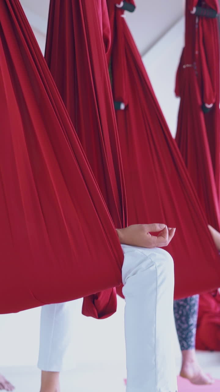 skilled fly yoga group sits in red hammocks and relaxes holding fingers in guan mudra meditation position close view
