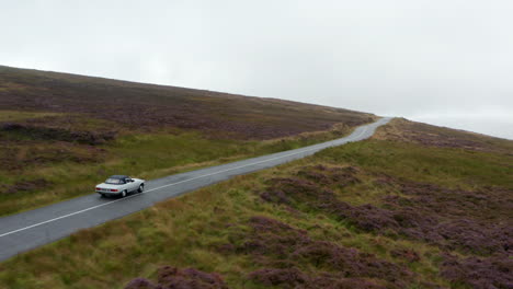 Forwards-tracking-of-vehicle-driving-on-wet-road-surrounded-by-grasslands-and-meadows.-Autumn-weather-with-overcast-sky.-Ireland