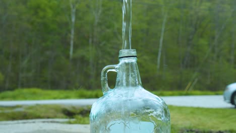 a firm young asian male hand holding a glass jug to get water from a public faucet