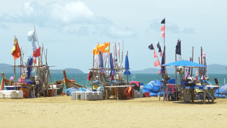 banderas de tela coloridas en postes de madera soplados por el viento en una playa junto a barcos atracados en la orilla del mar