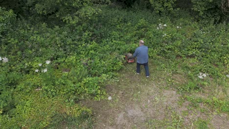 Aerial-view-of-an-older-man-using-a-mower-to-maintain-an-overgrown-garden