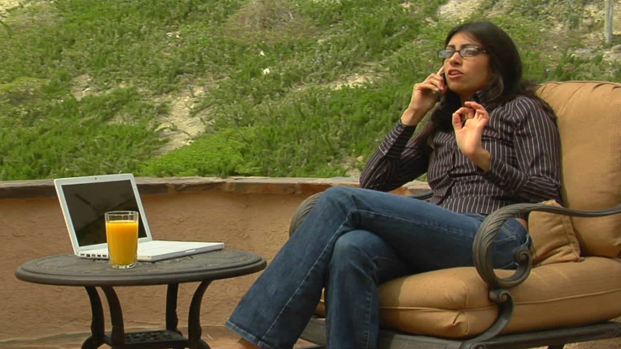 una mujer habla por un teléfono celular mientras está sentada en un patio