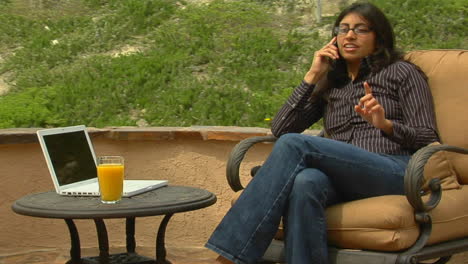 a woman speaks into a cell phone while sitting on a patio