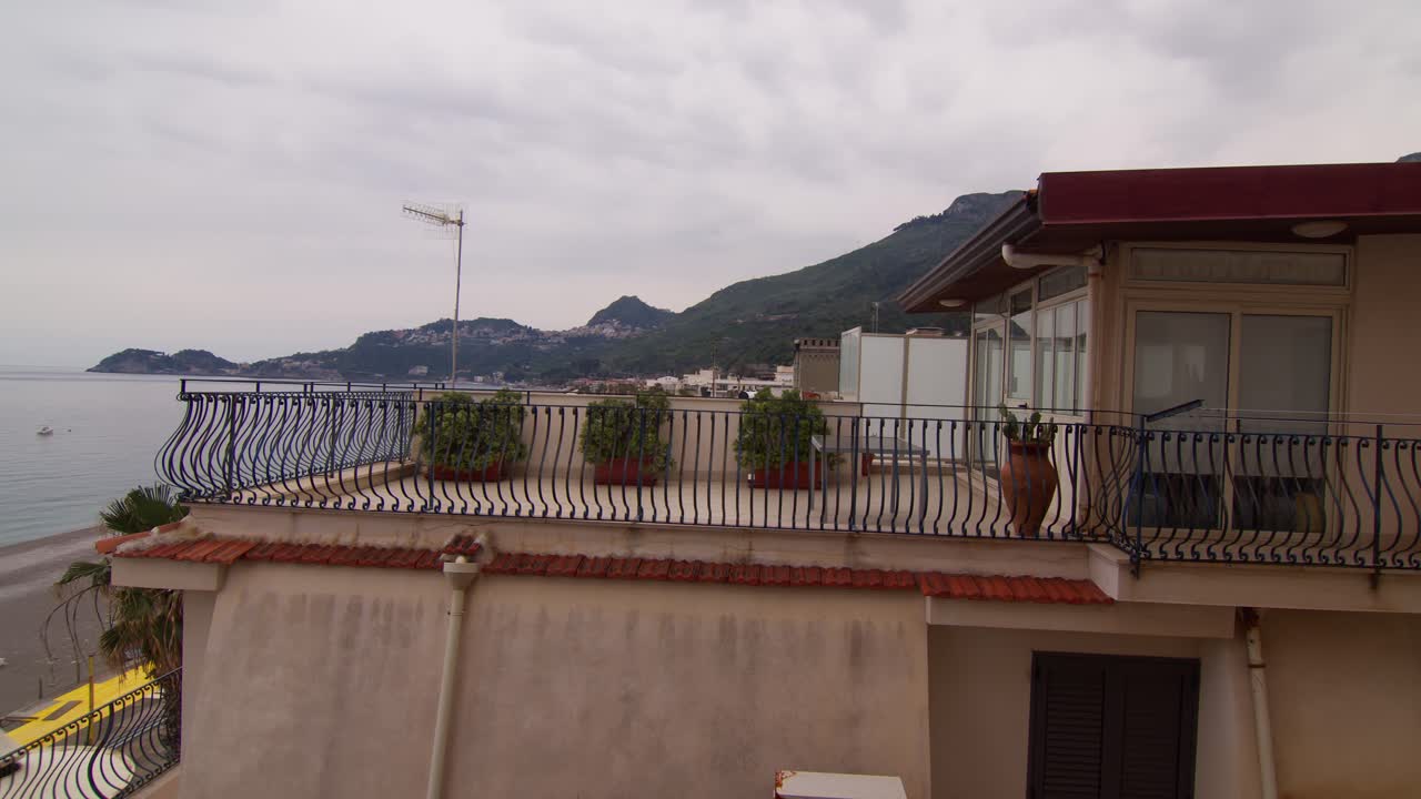 Panoramic view of a coastal rooftop terrace with potted plants overlooking a beach in Sicily