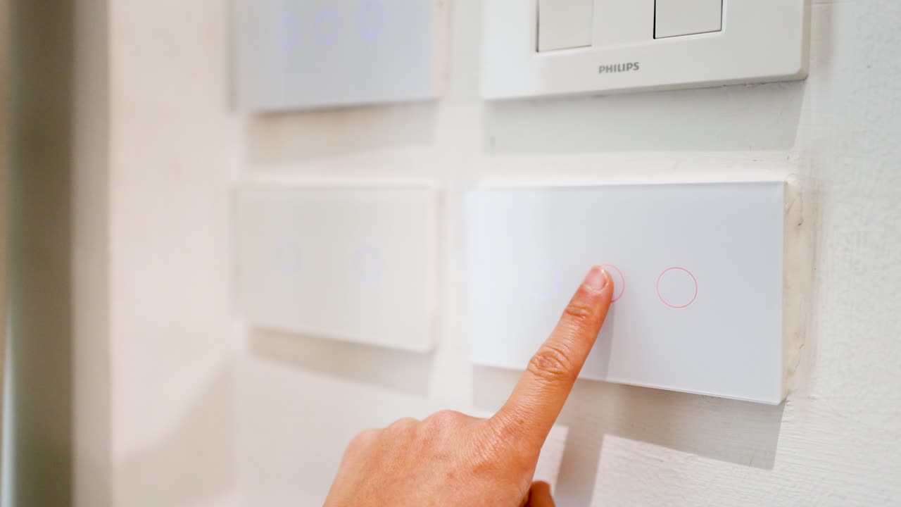 A finger presses buttons on a modern white touch panel to control smart home lighting