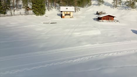 aerial view of smooth white snow landscape with dolly forward, tilt up reveal of buildings and hut in marebbe