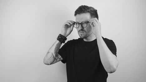 man with tattoos and poor eyesight puts on glasses to observe something by squinting and moving his head closer to what he is watching