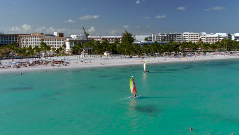 aerial capture of two sailboats passing in the tropical turquoise waters in front of a luxury resort, dominican republic