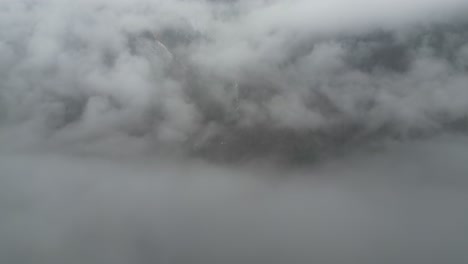 misty thick grey clouds shroud rugged mountain peak with snow in valley ridges