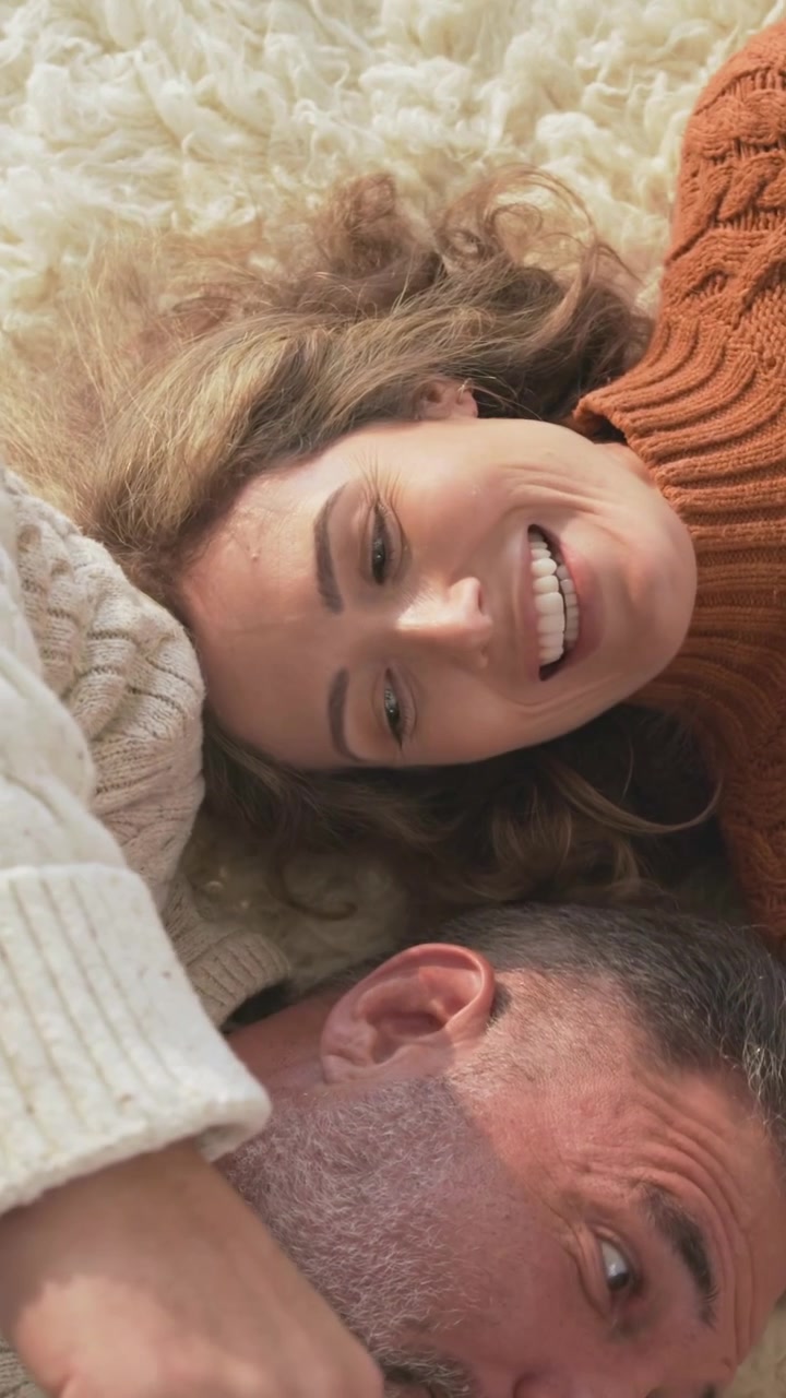 Vertical video: Smiling woman seeing dog, reaching to pet it for love on cream rug, in orange knit