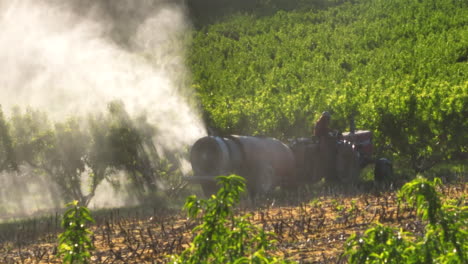 agricultor en tractor rocía productos químicos en árboles frutales