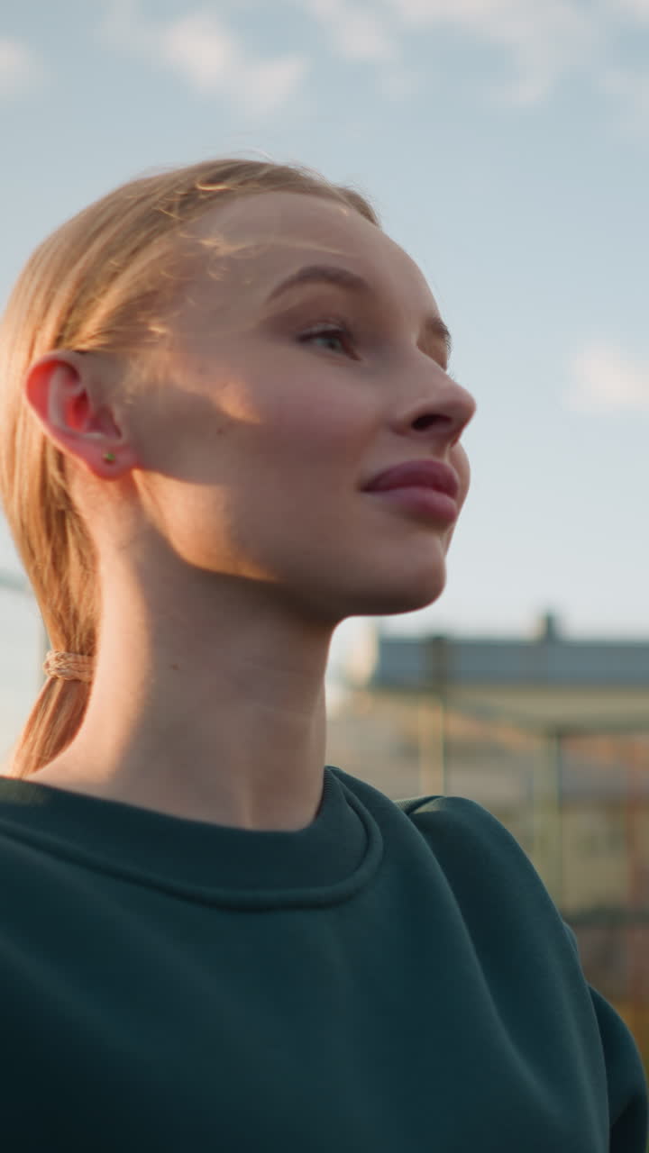 primer plano de una mujer con suéter verde jugando al voleibol con otra mujer con sueter azul borroso en el fondo, con un edificio y la luz del sol creando un brillo cálido