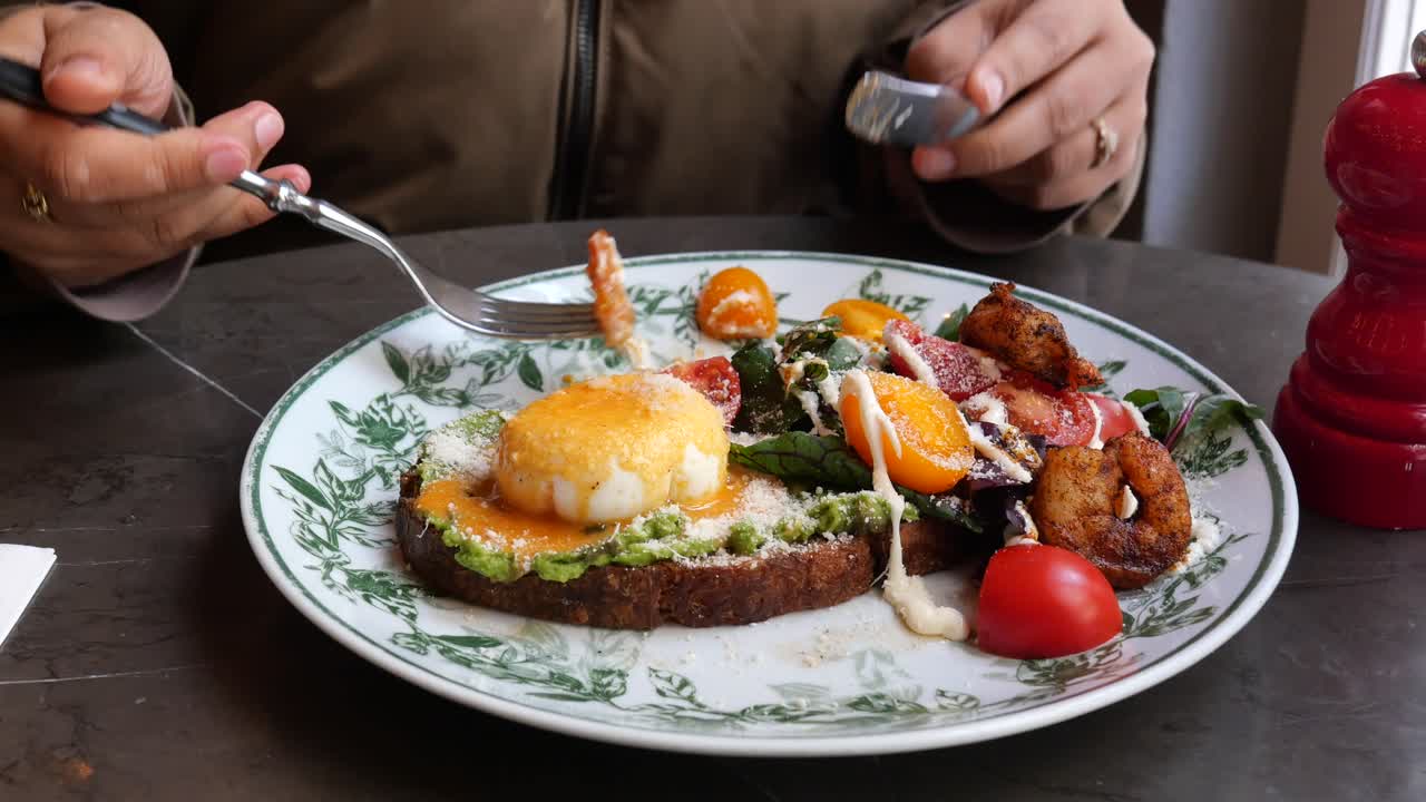 Woman Eating Avocado Toast with Poached Egg, Shrimp, and Salad