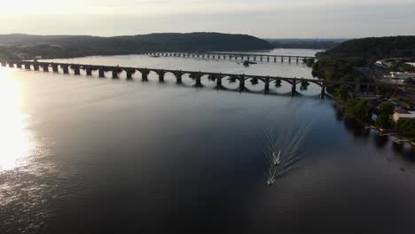 Cinematic-aerial-turn-of-sunset-at-Susquehanna-River-in-Pennsylvania,-boaters-leave-their-wake-with-bridges-at-Route-30-and-Route-462-span-Lancaster-and-York-Counties-in-Pennsylvania-USA