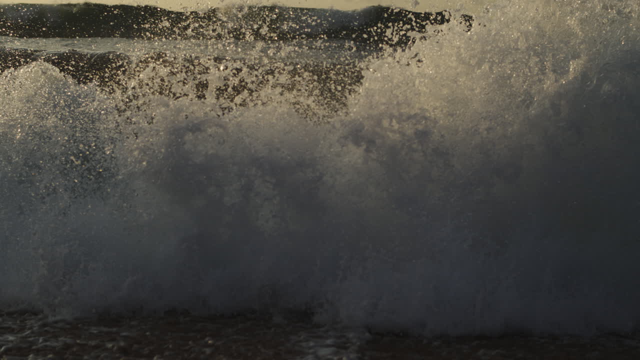 Churning wave pushes forward at shore with foamy textures in warm light