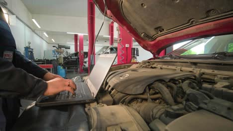 computer diagnostics of cars, young mechanic specialist male uses laptop technology while repairing vehicle with open hood at service station