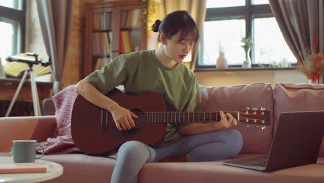 young asian woman learning guitar online at home