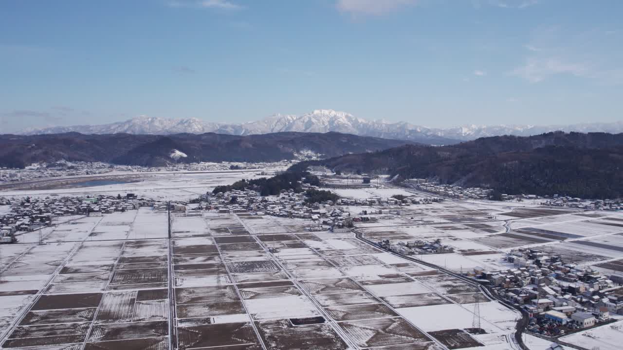 Drone ascending over the snow-covered countryside of Niigata, Japan, showing a scenic blend of nature, farms, and mountains