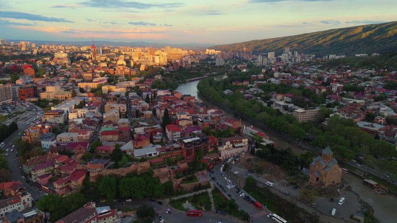 Letecký záběr dronem nad panoramatem města Tbilisi při západu slunce, hlavní město Gruzie během zlaté hodinky se starým městem.