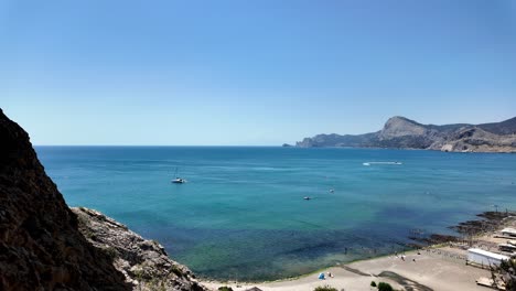 A-panoramic-view-of-the-Black-Sea-from-a-rocky-cliff,-with-a-beach-and-a-few-boats-in-the-distance