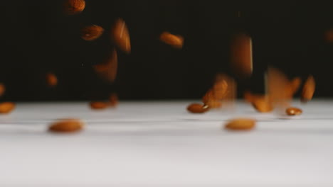 close up shot of almond nuts dropping onto marble surface against black studio background shot in slow motion