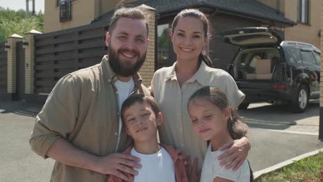 Familie-Mit-Zwei-Kindern,-Die-Zu-Hause-Im-Garten-In-Die-Kamera-Schauen-Und-Ein-Schild-Zum-Verkauf-Halten,-Um-In-Ein-Anderes-Haus-Zu-Ziehen