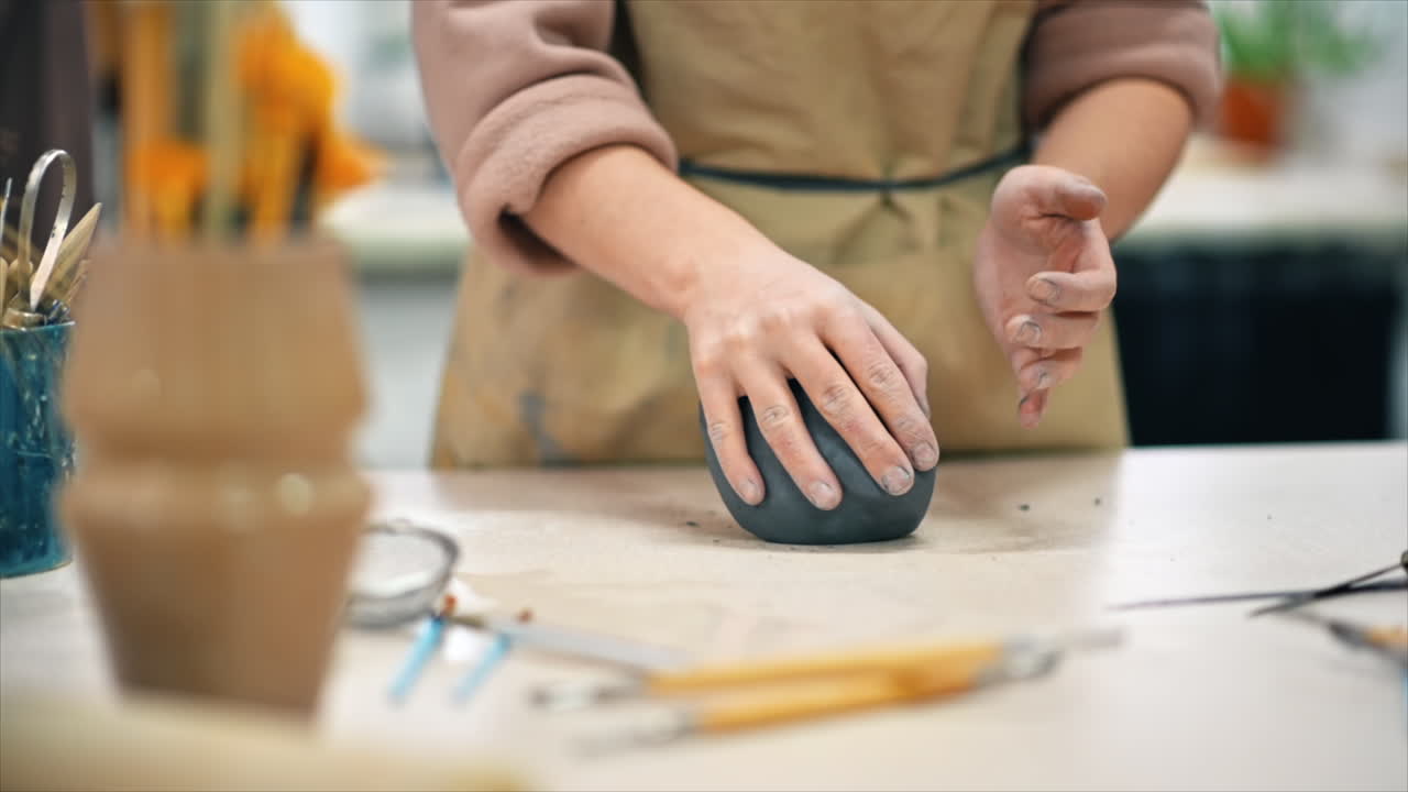 The master of sculpting pottery working in a studio. Kneading a piece of clay with her hands. Tools on the table. Slow motion