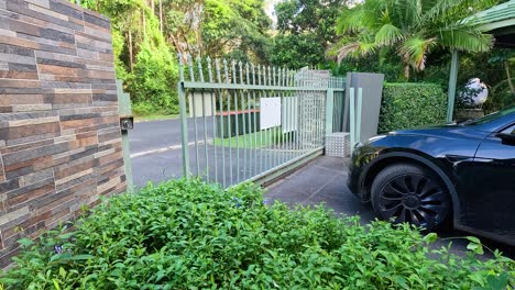 a black car approaches an automatic gate opening in a lush, sunlit driveway in coffs harbour, australia