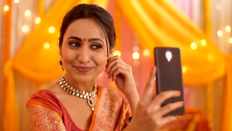 hermosa mujer india sonriendo y comprobando su cambio de aspecto mientras se toma una selfie durante el festival - concepto de tecnología
