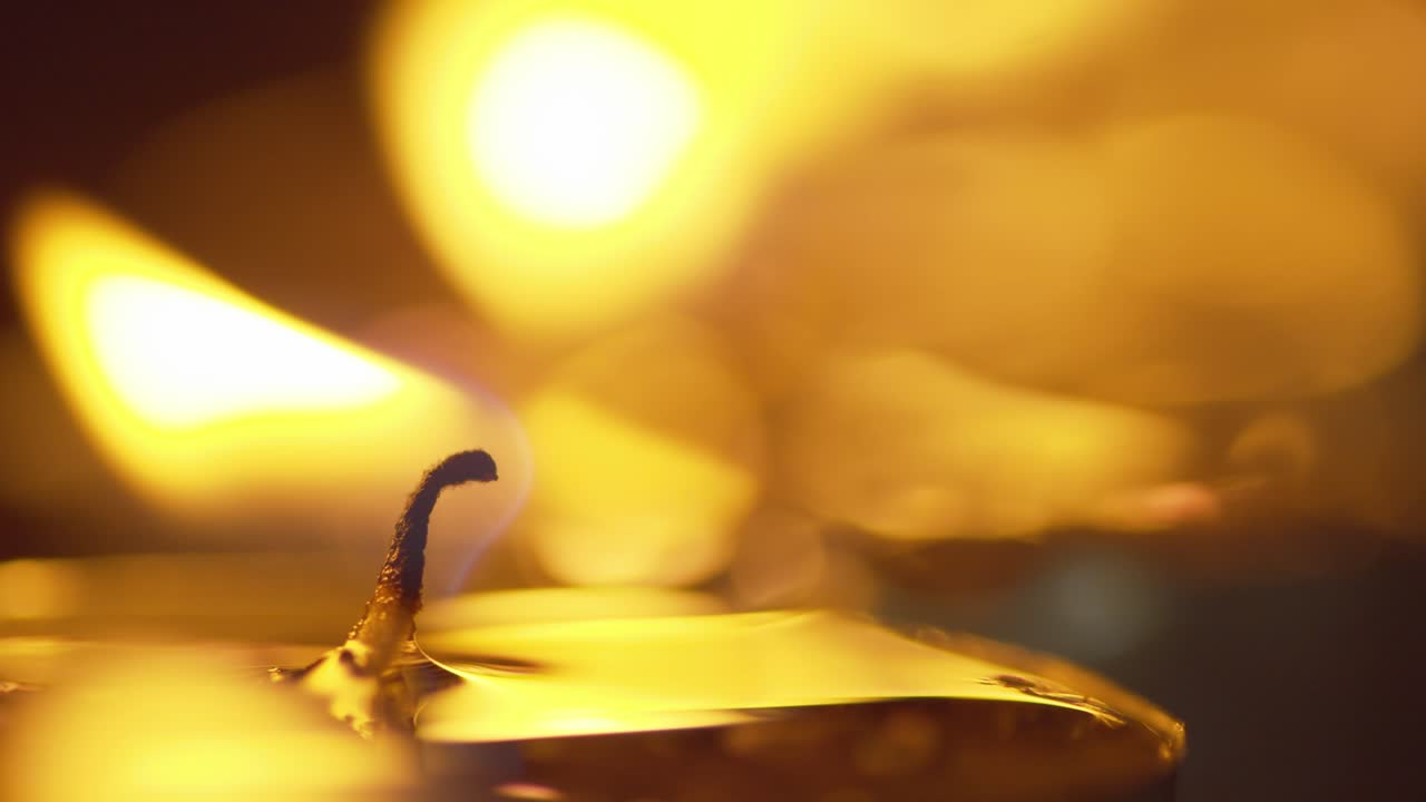 Static macro shot of a candle with a glowing flame - background candles shimmer with golden bokeh