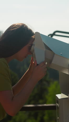 woman at observation deck using large binoculars to take in breathtaking views of mountains at popular tourist place. paid entertainment for tourists slow motion