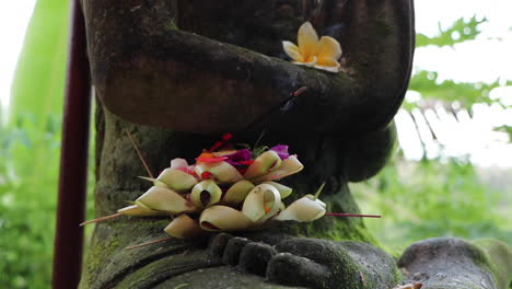 Hindu-Balinese-incense-sticks-and-offering-to-the-gods-with-flower-petals-and-statue-background