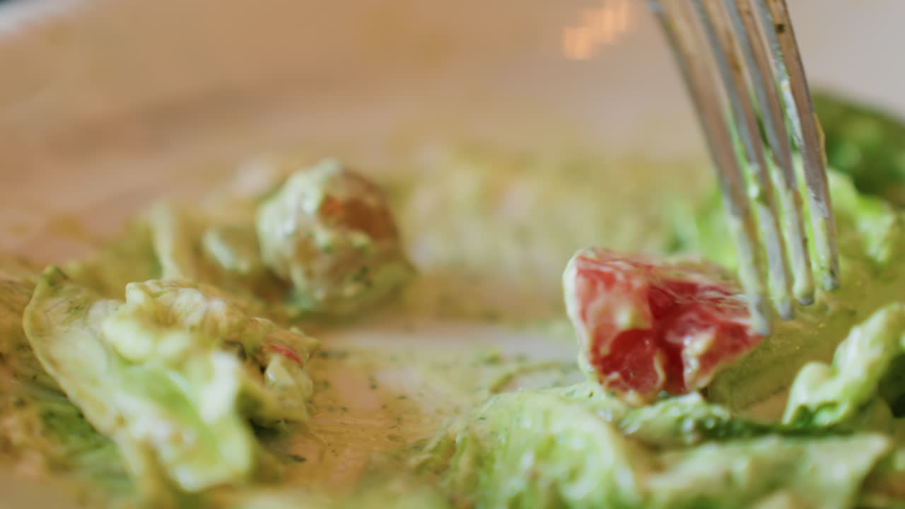 Macro closeup lettuce and tomato coated in creamy avocado dressing, fork probing cherry tomato and romaine, intimate food blogger tasting scene with shallow depth of field, vivid green textures
