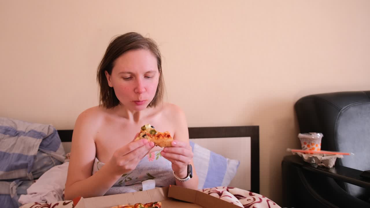 View of a circle of pizza lying in a crust on the lap of a girl who eats it with pleasure, at home.