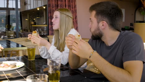 close up view of a woman and man talking and eating pizza with their friends at restaurant table 1