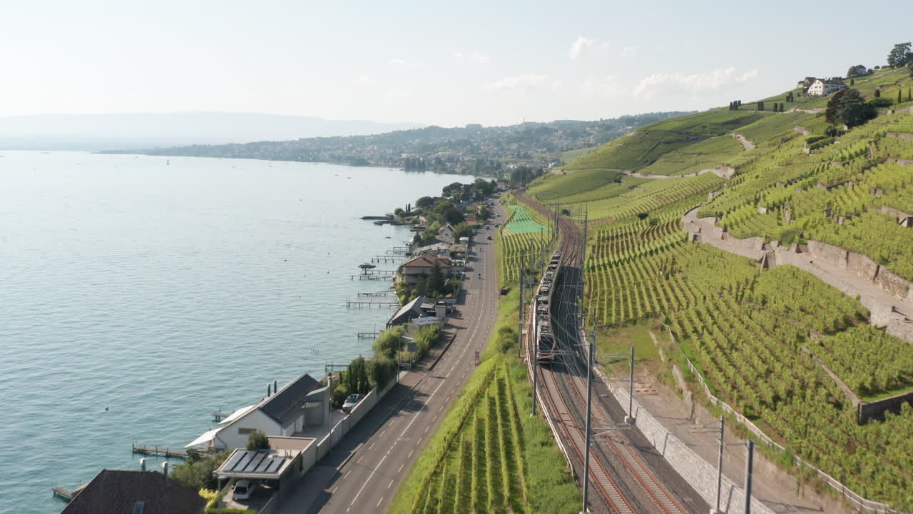 Aerial of train driving through beautiful Swiss landscape with hills and a large lake