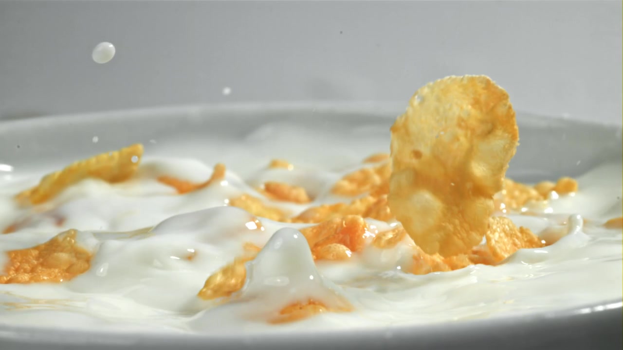 Cornflakes dorati che schizzano nel latte bianco fresco al rallentatore