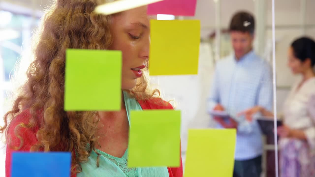 mujer ejecutiva mirando notas adhesivas mientras usa una computadora portátil
