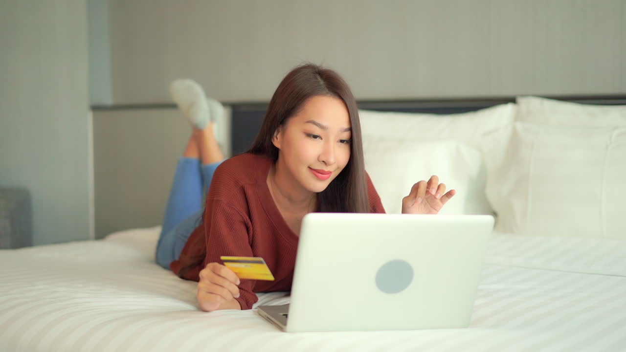 신용 카드와 노트북으로 침대에 누워 행복 한 아시아 여자