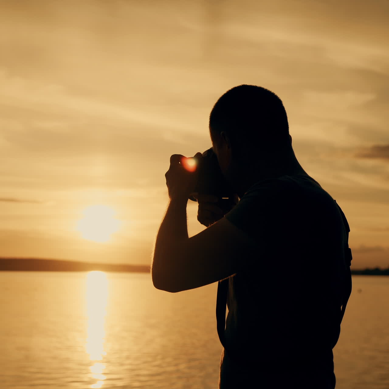 A man with a camera in his hands is photographing the sunset by the river on the background of people bathing. Close-up