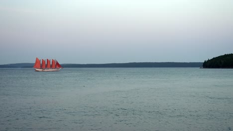 Bright-red-sails-on-multi-masted-tan-boat-separate-brilliantly-against-sunset-sky,-slow-motion