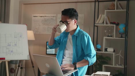 asian man engineer sitting on the table and drinking coffee while using a laptop to work at the office